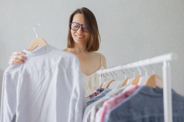Siyah saçlı ve gözlüklü Avrupalı bir kadın profesyonel stilist iş toplantısı veya akşam yemeği için kıyafet seçer. 