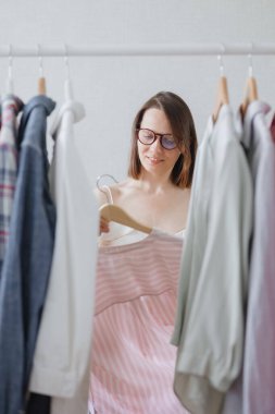 Siyah saçlı ve gözlüklü Avrupalı bir kadın profesyonel stilist iş toplantısı veya akşam yemeği için kıyafet seçer. 