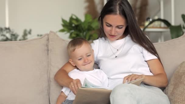 Ευρωπαϊκή οικογένεια μαμά και γιος παίζουν και να διαβάσετε ένα βιβλίο στο σπίτι. Η ανύπαντρη μητέρα μεγαλώνει ένα παιδί — Αρχείο Βίντεο