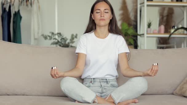 Egy európai nő otthon meditál a kanapén. egy sikeres nő otthon végez légzést és spirituális gyakorlatokat munka után, vagy jelentést és határidőt, hogy lenyugodjon, — Stock videók