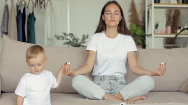 Avrupalı bir kadın evinde kanepede meditasyon yapıyor. Küçük bir çocuğun annesi manevi uygulamalara ve yogaya bağlıdır.