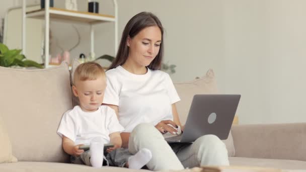 Ευτυχισμένη ανύπαντρη μητέρα και ο γιος είναι στο σπίτι με ένα φορητό υπολογιστή και ένα τηλέφωνο εργασίας. μητρότητα και επιχείρηση σε σύγχρονες συνθήκες — Αρχείο Βίντεο