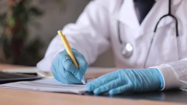 白いコートと医療用手袋の医者はノートにメモを作るか、患者に治療の予定を書いています。診療所や病院の医師療法士は — ストック動画
