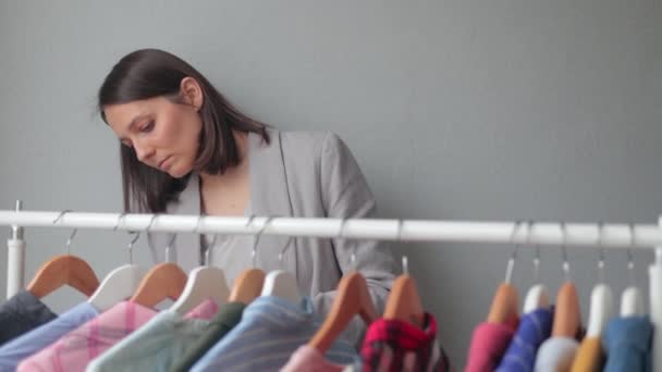 Vrouw kiest kleding op hangers in een garderobe of winkel. een Europese vrouw stylist pick-up kleding voor een zakelijke bijeenkomst of een datum — Stockvideo