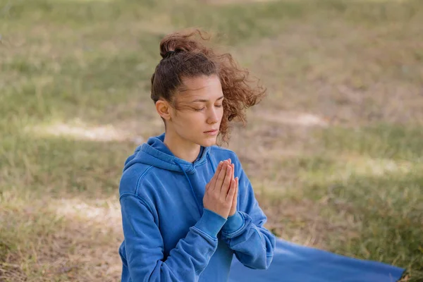 Frau mit lockigem Haar meditiert in einem Park. Yoga und Meditation für geistige und körperliche Gesundheit — Stockfoto
