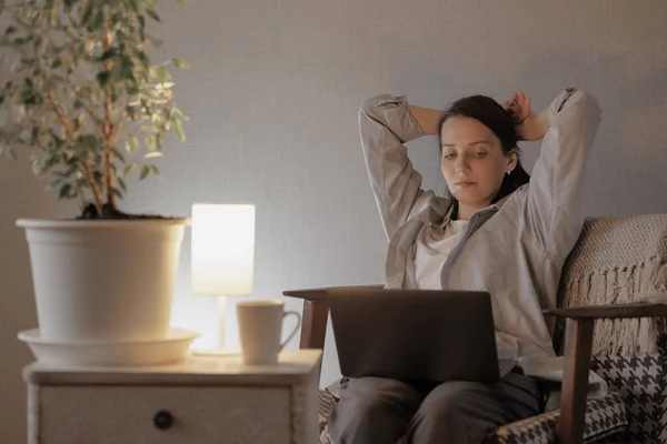 Γυναίκα στο σπίτι εργάζεται σε ένα φορητό υπολογιστή σε μια ζεστή πολυθρόνα. Ευρωπαίος επιχειρηματίας ή τύπος σπουδαστή σε φορητό υπολογιστή τη νύχτα ή το βράδυ — Φωτογραφία Αρχείου