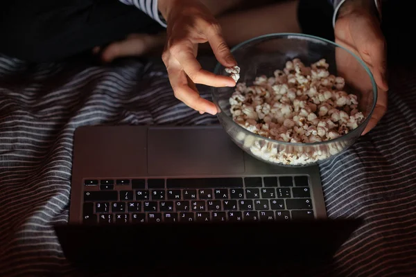 Vrouw in een gestreepte sweater en hoed eet popcorn en kijkt een film op tv of een tv-serie thuis vanaf een laptop — Stockfoto