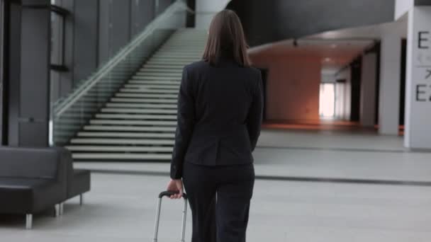 Donna d'affari in un abito da lavoro con una valigia cammina attraverso l'aeroporto o il business center e parla al telefono. una donna europea fiduciosa — Video Stock
