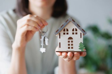 Kadın emlakçı ya da ipotek acentesi evin minyatürünü ve anahtarlarını elinde tutuyor. Emlak dairelerinin ya da bahçeli evlerin satışı ve alımı