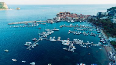 Karadağ 'ın Budva kentindeki tekne rıhtımı ve yat limanının havadan aşağı görüntüsü. Beyaz özel motorlu tekneler Adriyatik deniz kıyısındaki iskeleye demirlemiş. Yat tekneleri park ediyor. Fotoğraf: İHA.