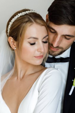 Şık bir damat, gelinlik giymiş bir gelini kucaklıyor. Yeni evliler odada kucaklaşıp birlikte vakit geçiriyorlar.