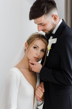 Şık bir damat, gelinlik giymiş bir gelini kucaklıyor. Yeni evliler odada kucaklaşıp birlikte vakit geçiriyorlar.