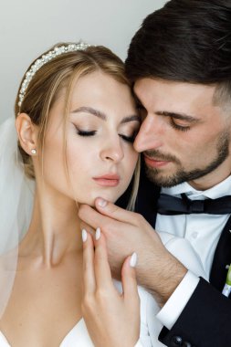 Şık bir damat, gelinlik giymiş bir gelini kucaklıyor. Yeni evliler odada kucaklaşıp birlikte vakit geçiriyorlar.