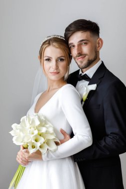 Şık bir damat, gelinlik giymiş bir gelini kucaklıyor. Yeni evliler odada kucaklaşıp birlikte vakit geçiriyorlar.