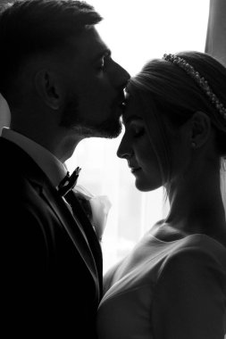 Şık bir damat, gelinlik giymiş bir gelini kucaklıyor. Yeni evliler odada kucaklaşıp birlikte vakit geçiriyorlar.