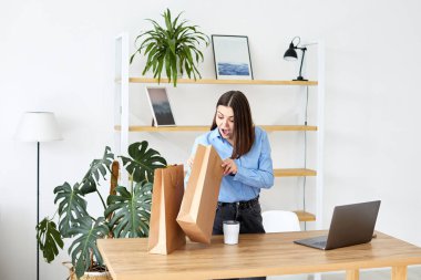 Happy young woman looking at paper bag and smiling.