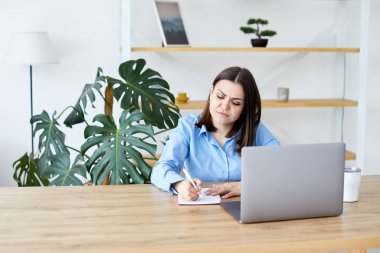 Konsantre iş kadını evdeki masada dizüstü bilgisayarla otururken evrak hazırlıyor.