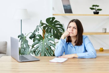 Genç bir kadın masada oturuyor ve dizüstü bilgisayarla çalışıyor..