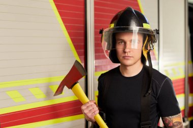 İtfaiyeci kasklı ve baltayla itfaiye arabasının karşısında.. 