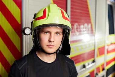 Young fireman in uniform standing in front of firetruck