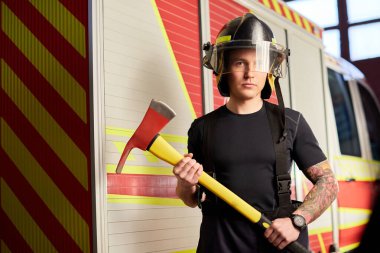 İtfaiyeci kasklı ve baltayla itfaiye arabasının karşısında.. 