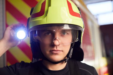 İtfaiye arabasının önünde duran üniformalı genç itfaiyeci.