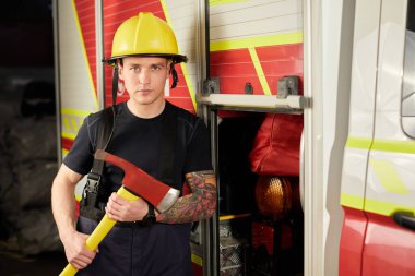 İtfaiyeci kasklı ve baltayla itfaiye arabasının karşısında.. 