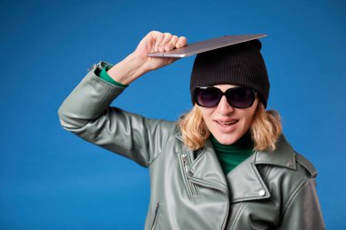 Başının üstünde boş ekranı olan dijital tableti tutan ve mavi arka planda çığlık atan genç bir kadın.