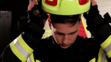Portrait shot of the Caucasian joyful firefighter taking on helmet with flashlight and looking confidently at the camera at the truck 
