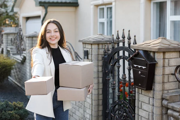 Kız evin yanında duruyor, elinde kutular ve kameranın önünde bir kutu tutuyor.