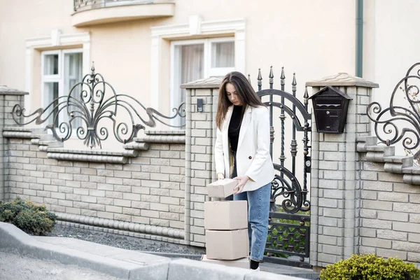 Elinde bir yığın karton kutuyla eve paket taşıyan genç bir kadın..