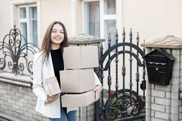 Elinde bir yığın karton kutuyla eve paket taşıyan genç bir kadın..