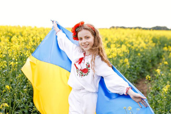 Pray for Ukraine. Child with Ukrainian flag in rapeseed field. Girl holding national flag praying for peace.