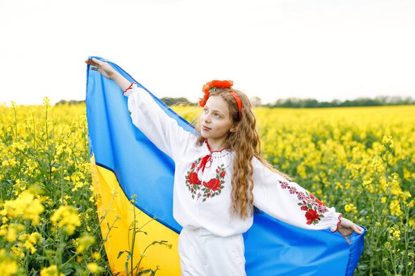 Pray for Ukraine. Child with Ukrainian flag in rapeseed field. Girl holding national flag praying for peace.