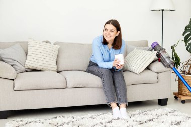 Charming brunette housewife enjoying time of the rest at home after cleaning carpet with modern vacuum