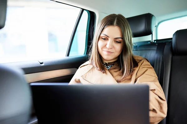 Attractive business woman working on her laptop at the back sit of a car on the way to meeting