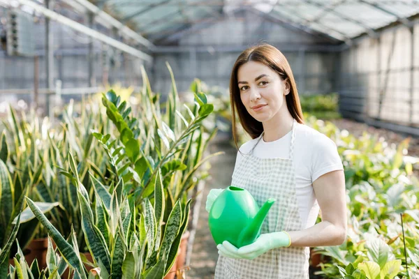 Genç bir kadın büyük bir seranın ortasında elinde bir su bidonuyla kameraya gülümsüyor.
