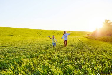 Koşan çocuk ve kız ellerinde iki sarı ve mavi uçak oyuncağı yaz güneşli bir günde tarlada