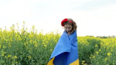Ukrayna için dua et. Kolza tarlasında Ukrayna bayrağı taşıyan bir çocuk. Ulusal bayrak tutan kız barış için dua ediyor.