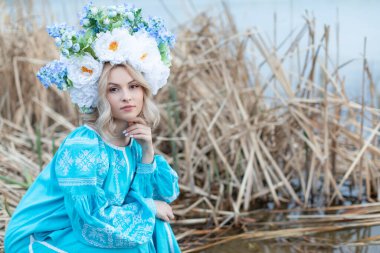 Ukraynalı güzel bir kadın mavi işlemeli bir elbise giymişti. Kafasında büyük güzel bir çiçek çelengi vardı. Elleriyle çenesine dokunuyordu ve kameraya bakıyordu.. 