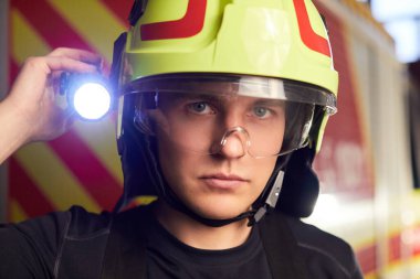 İtfaiye arabasının önünde duran üniformalı genç itfaiyeci.