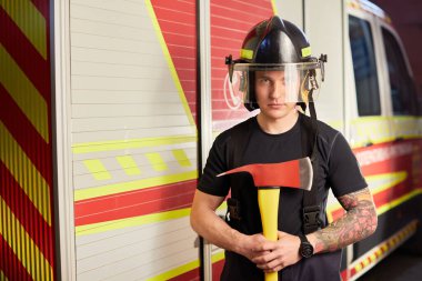 İtfaiyeci kasklı ve baltayla itfaiye arabasının karşısında.. 