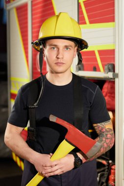 İtfaiyeci kasklı ve baltayla itfaiye arabasının karşısında.. 