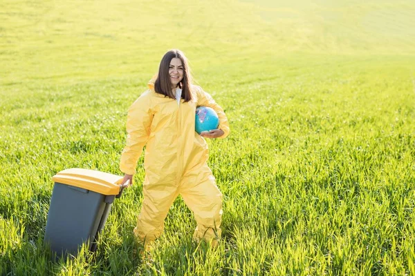 Woman Yellow Protective Suit Stands Middle Green Field Holding Globe — Stock Photo, Image