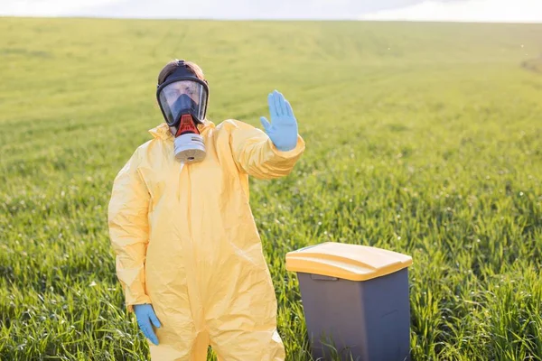 Sarı koruyucu takım elbiseli bir kadın yeşil bir tarlanın ortasında koruyucu gaz maskeli bir şekilde duruyor ve durup gezegeni kurtarmak için bir jest yapıyor. Bir kadın çöp tenekesinin yanında duruyor ve gezegeni kurtarmak için bağırıyor.
