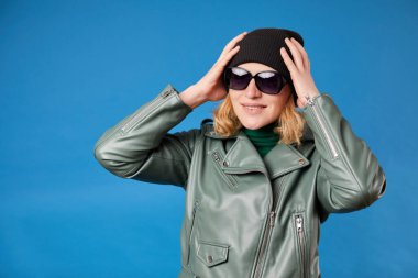 Siyah şapkalı neşeli kız ellerini şakacı bir şekilde kafasında tutuyor, eğlenceli gülüyor, yeşil ceket giyiyor.