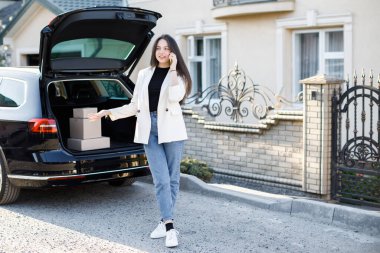 Genç iş kadını elinde paketlerle arabada duruyor, arabayla eve geliyor. Kız arabanın yanında duruyor ve elinde bir cep telefonu var..