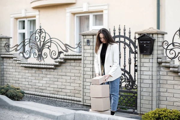 Elinde bir yığın karton kutuyla eve paket taşıyan genç bir kadın..
