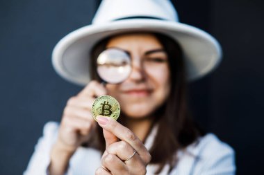 Beyaz şapkalı zarif iş kadını elinde büyüteçle Bitcoin 'e bakıyor..