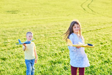 Koşan çocuk ve kız ellerinde iki sarı ve mavi uçak oyuncağı yaz güneşli bir günde tarlada